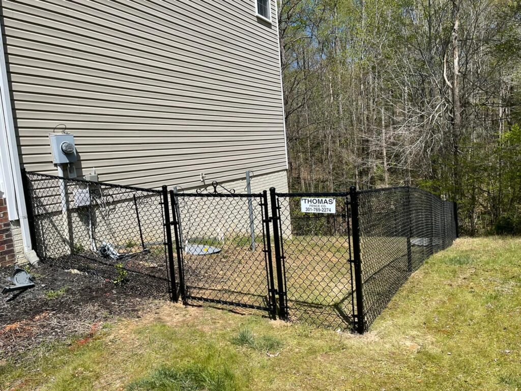 Black chain link fence with a walk gate beside a house