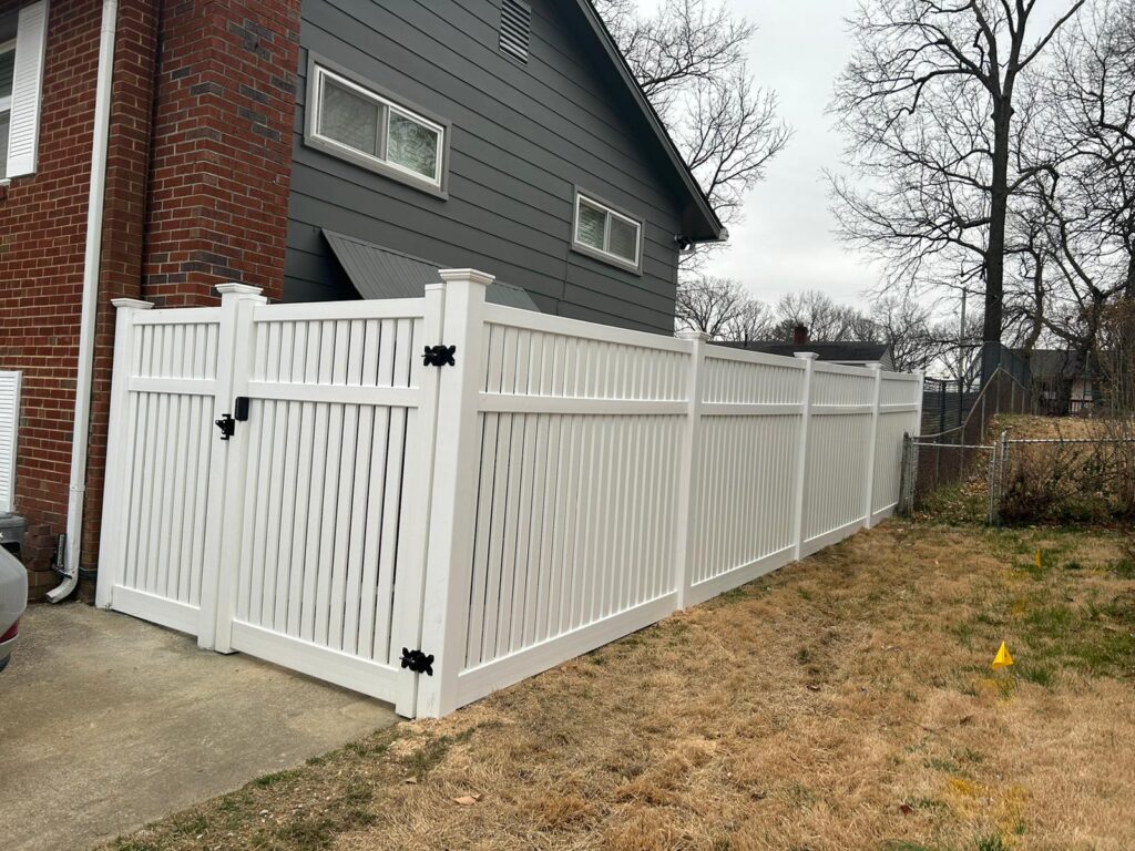 White vinyl fence and gate beside a brick home