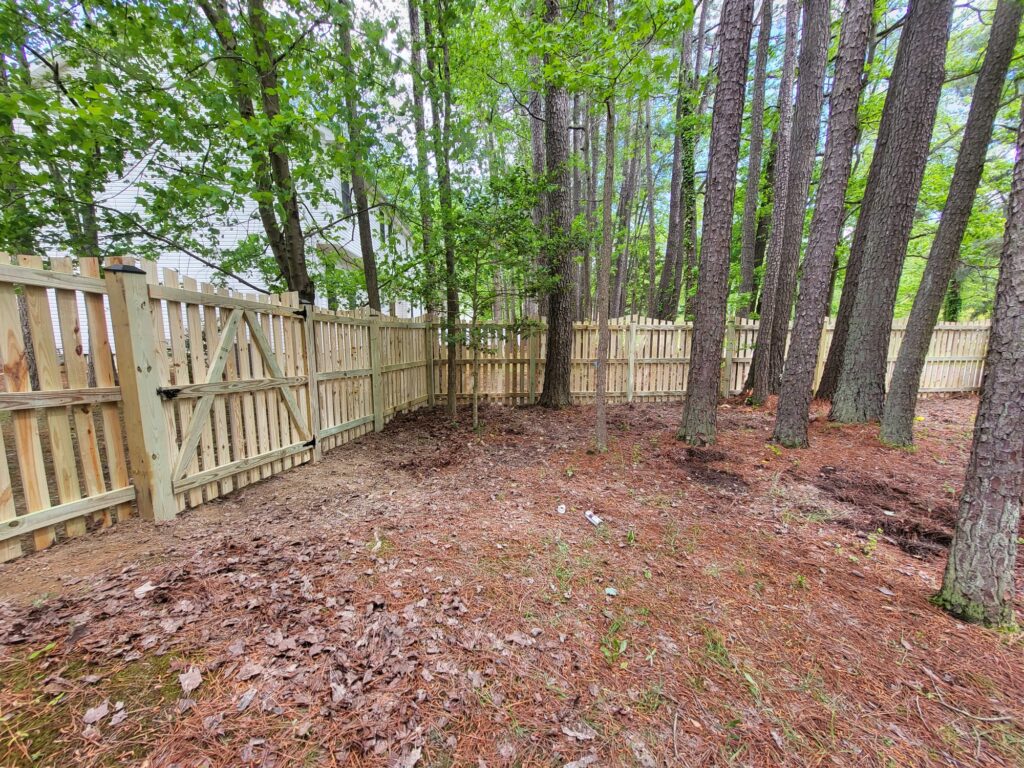 Wood picket fence running through a wooded backyard