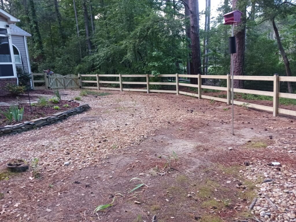 Wood post and rail fence around a mulched backyard