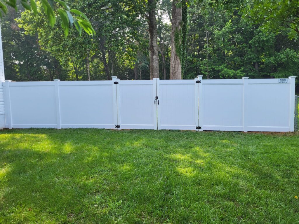 White vinyl privacy fence with a double gate across a backyard