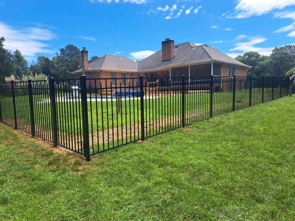 Black aluminum fence corner with a brick home and pool in the background