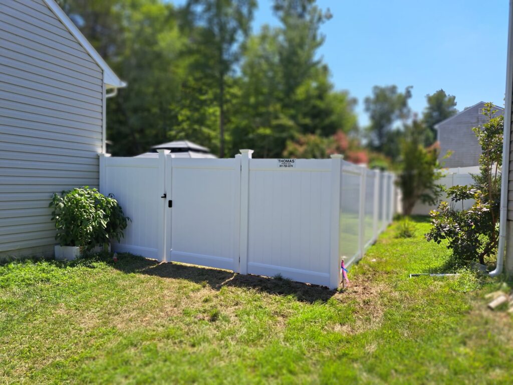 White vinyl privacy fence with a gate beside a house