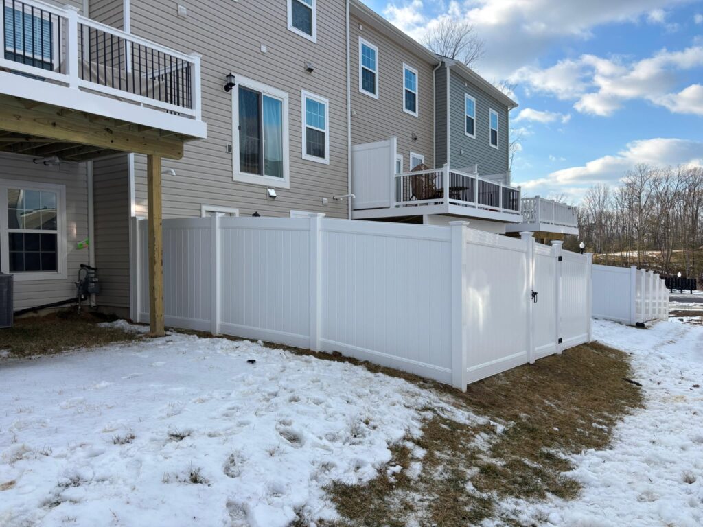 White vinyl privacy fence behind townhouses after a light snow