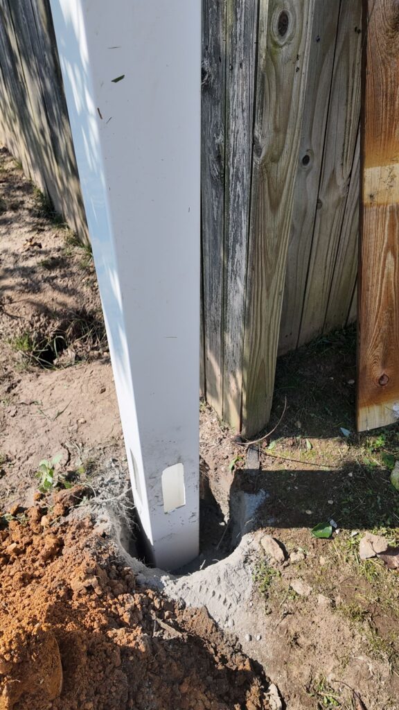 New white vinyl fence post set next to an old wood fence
