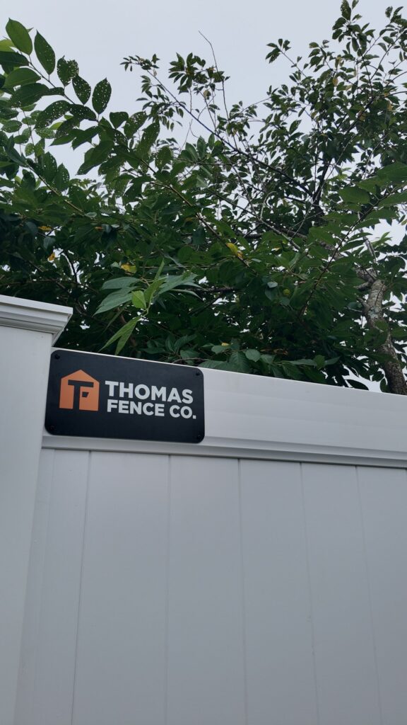 Thomas Fence Co sign on a new white vinyl privacy fence